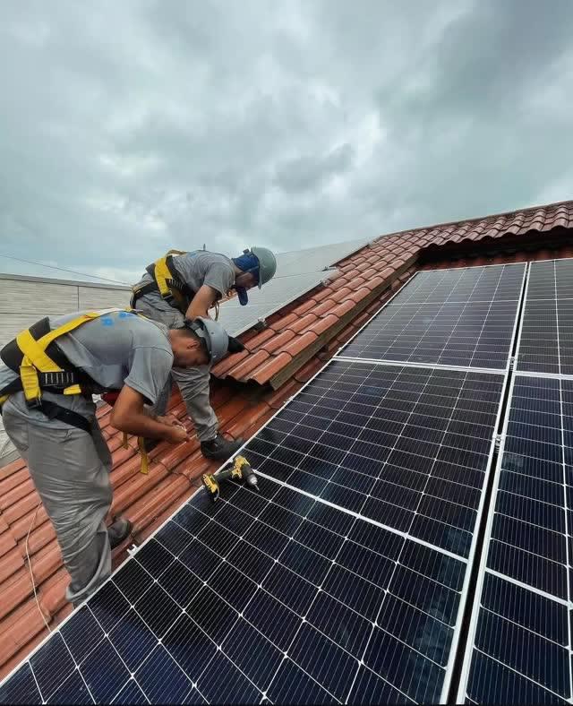 Dois técnicos da Ophir fixando painel solar em telha colonial, um deles com cinto de segurança
